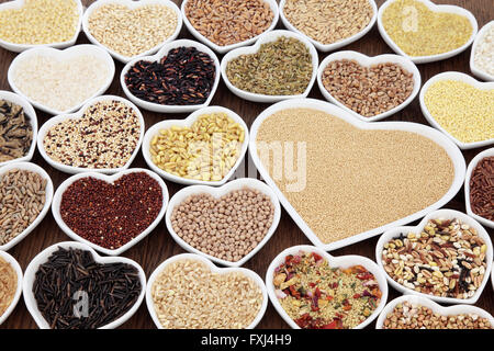 Large cereal and grain food selection in heart shaped porcelain bowls over lokta paper background. Amaranth in the largest dish. Stock Photo