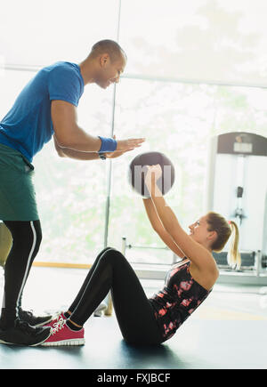 Personal trainer guiding woman with medicine ball at gym Stock Photo