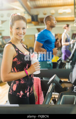 Portrait smiling woman with water bottle on treadmill at gym Stock Photo