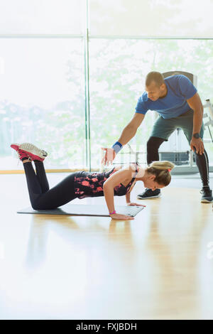 Personal trainer guiding woman doing push-ups on knees at gym Stock Photo