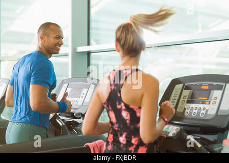 Man and woman talking and running on treadmills at gym Stock Photo
