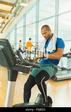 Man checking smart watch on exercise bike at gym Stock Photo