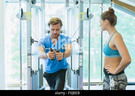 Personal trainer guiding man using cable exercise machine at gym Stock Photo
