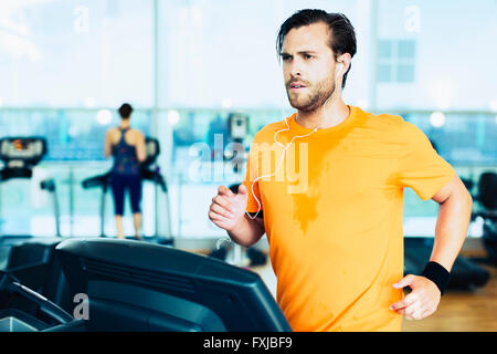 Sweating man with headphones running on treadmill at gym Stock Photo