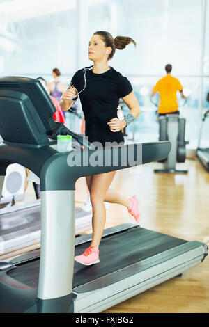 Woman running on treadmill with headphones at gym Stock Photo