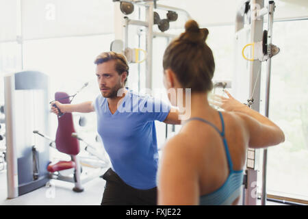 Female personal trainer guiding man doing cable chest fly at gym Stock Photo