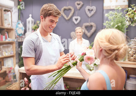 Florist tying flowers for woman in flower shop Stock Photo