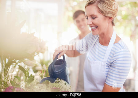 Smiling florist watering flowers in flower shop Stock Photo