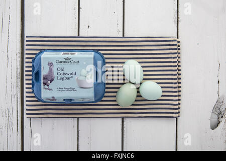 Old Cotswold Legbar Free range eggs with pastel coloured shells in a box on a blue and white striped napkin over rustic table Stock Photo