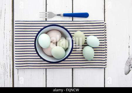 Old Cotswold Legbar Free range eggs with pastel coloured shells in a bowl on a blue and white striped napkin over rustic table Stock Photo