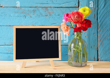 flowers next to empty blackboard, on wooden table. copy space Stock Photo
