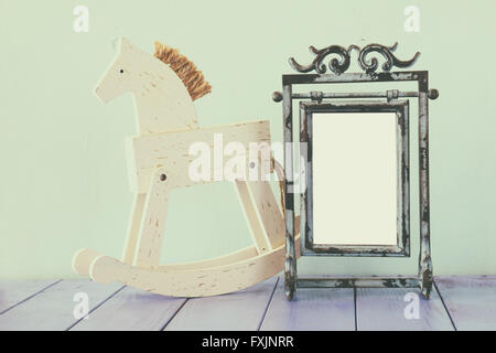 Antique blank vintage style frame and old rocking horse over wooden table. Stock Photo