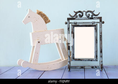 Antique blank vintage style frame and old rocking horse over wooden table. Stock Photo