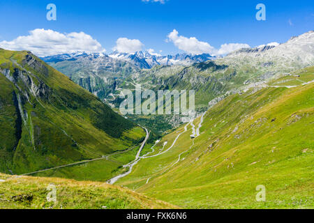 Road leading to Furka Pass winding up a green mountain slope, high mountains in the distance, Andermatt, Uri, Switzerland Stock Photo