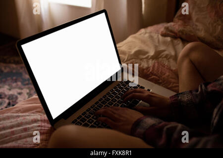 Woman sitting on bed and using laptop Stock Photo