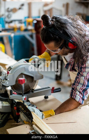 Carpenter cutting wooden plank with electric saw Stock Photo