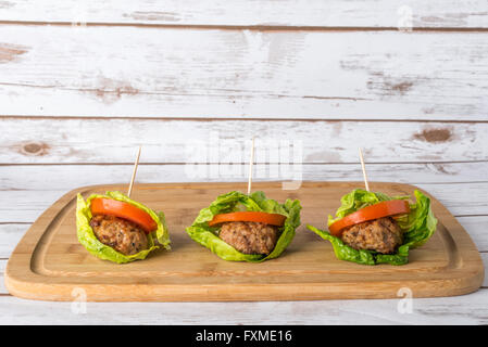 Bunless burger with bun replaced with lettuce leaves on wooden board Stock Photo