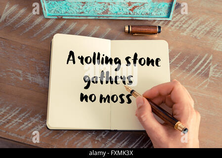 Retro effect and toned image of a woman hand writing on a notebook. Handwritten quote A rolling stone gathers no moss as inspirational concept image Stock Photo