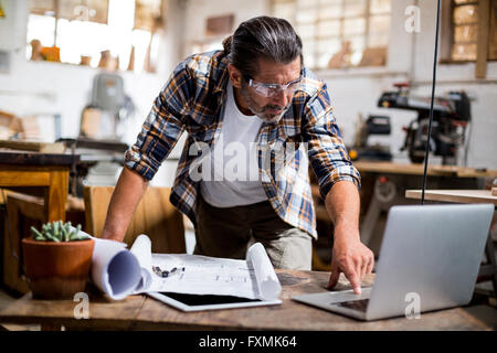 Carpenter using laptop while working on blueprint Stock Photo
