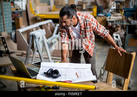 Carpenter looking at laptop while working on blueprint Stock Photo