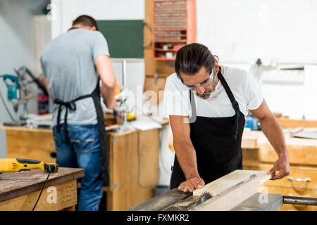 Carpenter using table saw for cutting wood at workbench Stock Photo