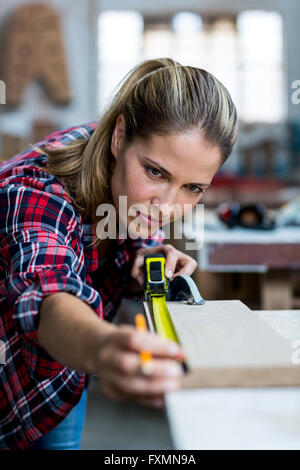 Female carpenter measuring length of wooden plank Stock Photo
