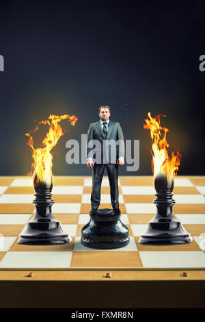 Businessman standing on the chess board instead of a pawn between two blames Stock Photo