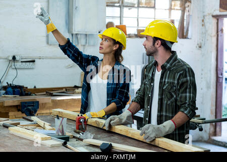 Male and female carpenter looking up and pointing while working Stock Photo