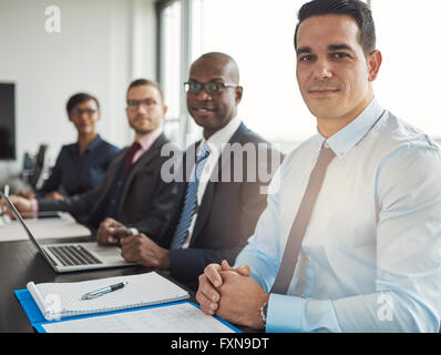 Calm diverse group of four business people sitting at table with computer and notebooks in front of large office window with lig Stock Photo