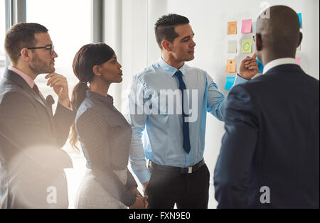 Multiracial group of businesspeople standing discussing colorful memos on a wall in a concept of teamwork and cooperation Stock Photo