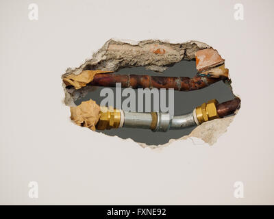 metal  pipes and fittings of domestic water supply system seen through a hole in a white wall Stock Photo