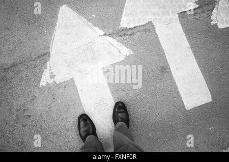 Male feet in new black shining leather shoes stand on asphalt pavement with white arrows pedestrian crossing road marking, first Stock Photo