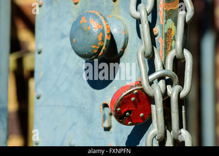 Red padlock and chain on an iron gate with knob in background.