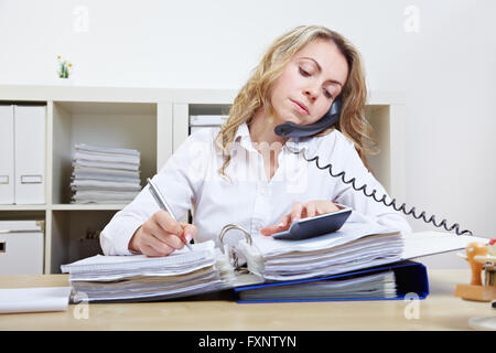 Busy business woman on the phone taking notes and using a calculator Stock Photo