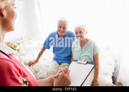 Nurse writing on clipboard and senior couple sitting on a bed Stock Photo