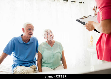 Nurse writing on clipboard and senior couple sitting on a bed Stock Photo
