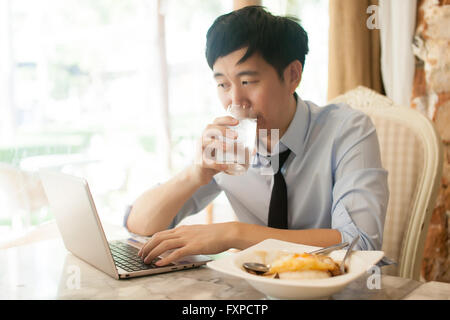 Young Asian man working while eating with his laptop in restaurant Stock Photo