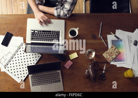 Man using laptop computer on desk cluttered with documents Stock Photo