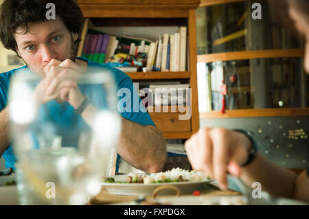 Man sitting at dinner table with hands clasped in front of his mouth Stock Photo
