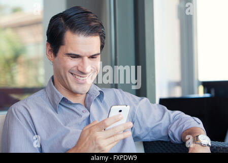 Man using smartphone and smiling cheerfully Stock Photo