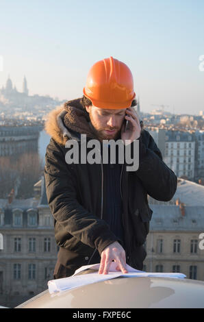 Construction supervisor talking on cell phone and looking at blueprints Stock Photo