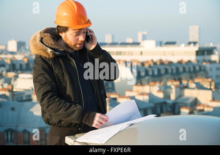 Construction supervisor studying blueprints and talking on cell phone Stock Photo