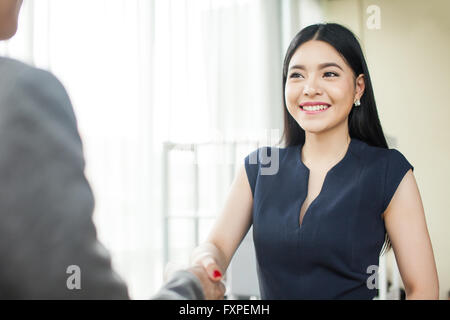 Beautiful Asian businesswoman smiling and shaking hands with other businessman Stock Photo