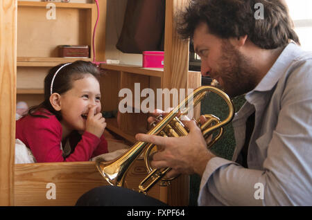 Father playing trumpet for little girl lying in bed Stock Photo