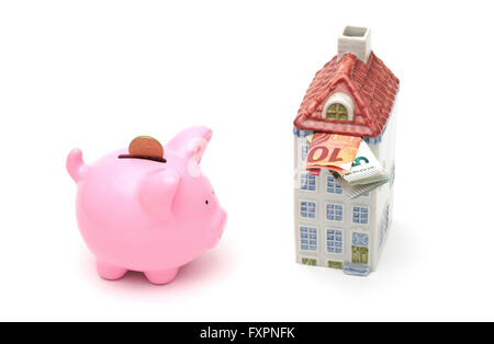 A money box in the shape of a house filled with euro notes next to a piggy bank Stock Photo