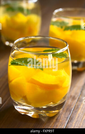 Refreshing peach, lemon balm and white wine punch or wine cooler in glasses, photographed on dark wood with natural light Stock Photo
