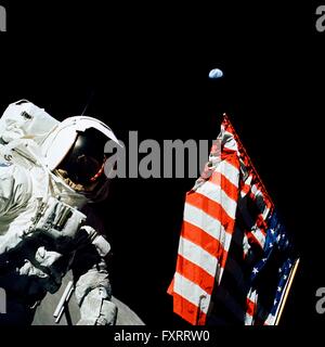 NASA Apollo 17 astronaut and scientist Harrison Schmitt stands next to the American flag during the first EVA on the lunar surface with the earth seen in the distance December 12, 1972. Apollo 17 is the final lunar landing mission scheduled. Stock Photo