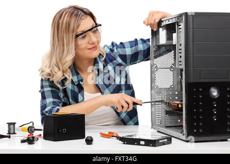 Young blond woman fixing a desktop computer seated at a table isolated on white background Stock Photo