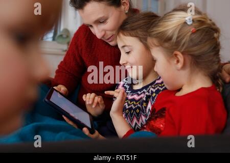 Mother and daughters on sofa sitting using digital tablet smiling Stock Photo