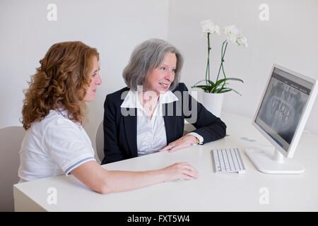 Senior woman and mature woman at desk discussing x-ray image on computer screen smiling Stock Photo